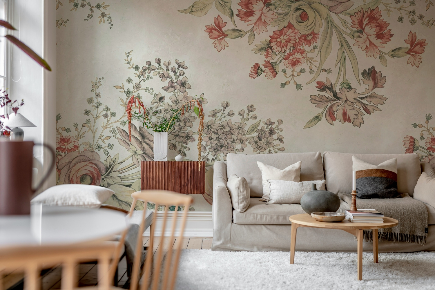 Bold and large floral mural wallpaper in pink featured in living room, styled with grey linen sofa and natural wood furniture.