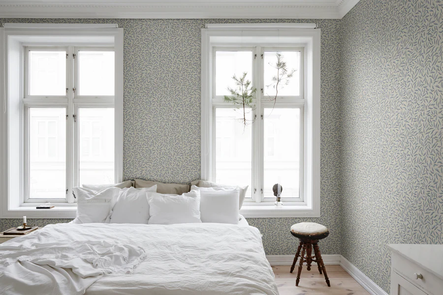 Karolina Foliage, Pattern Wallpaper in sage featured on a wall of a bedroom with full white bed sheet and two large windows