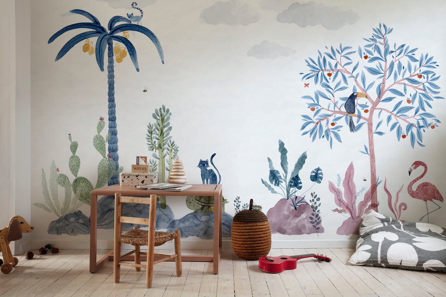 Whimsical tropical playroom wallpaper with illustrated palm trees, animals, and soft pastel foliage behind a wooden kids’ table and toys