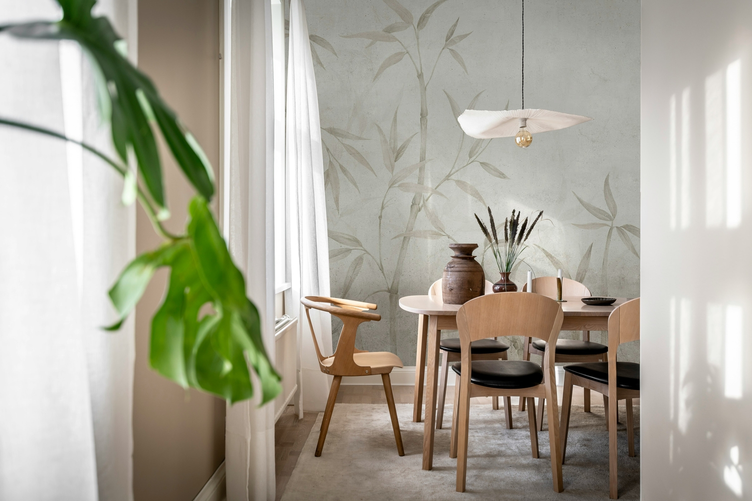 Dining room with light wood furniture and a neutral bamboo wallpaper mural, styled with natural décor and soft daylight through sheer curtains.